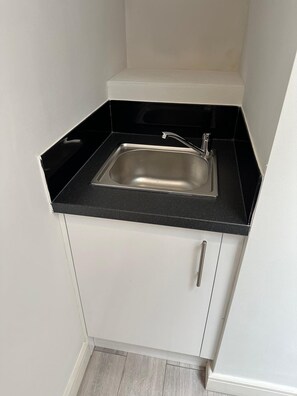 Eine kleine Küche mit schwarzem Arbeitsplatz, einer Edelstahl-Spüle und weißen Schränken.