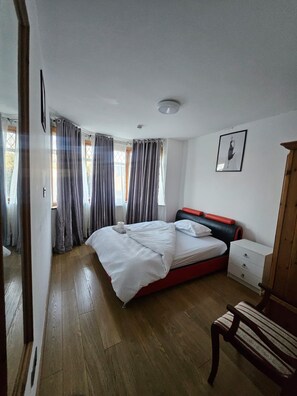 A bedroom with a bed, a bedside table, a chair, and a wardrobe. - House Sleeps 10 with Hot Tub and Garden (Romford)