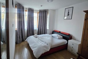 Un dormitorio con cama, mesita de noche, cómoda y un cuadro enmarcado en la pared.