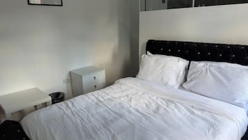 A bedroom with a bed, a nightstand, a trash bin, and a wall-mounted picture.
