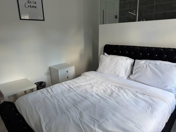A bedroom with a bed, a nightstand, a trash bin, and a wall-mounted picture.