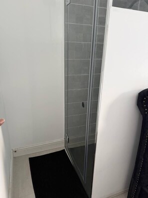 A bathroom with a shower area, a door, and a black mat.