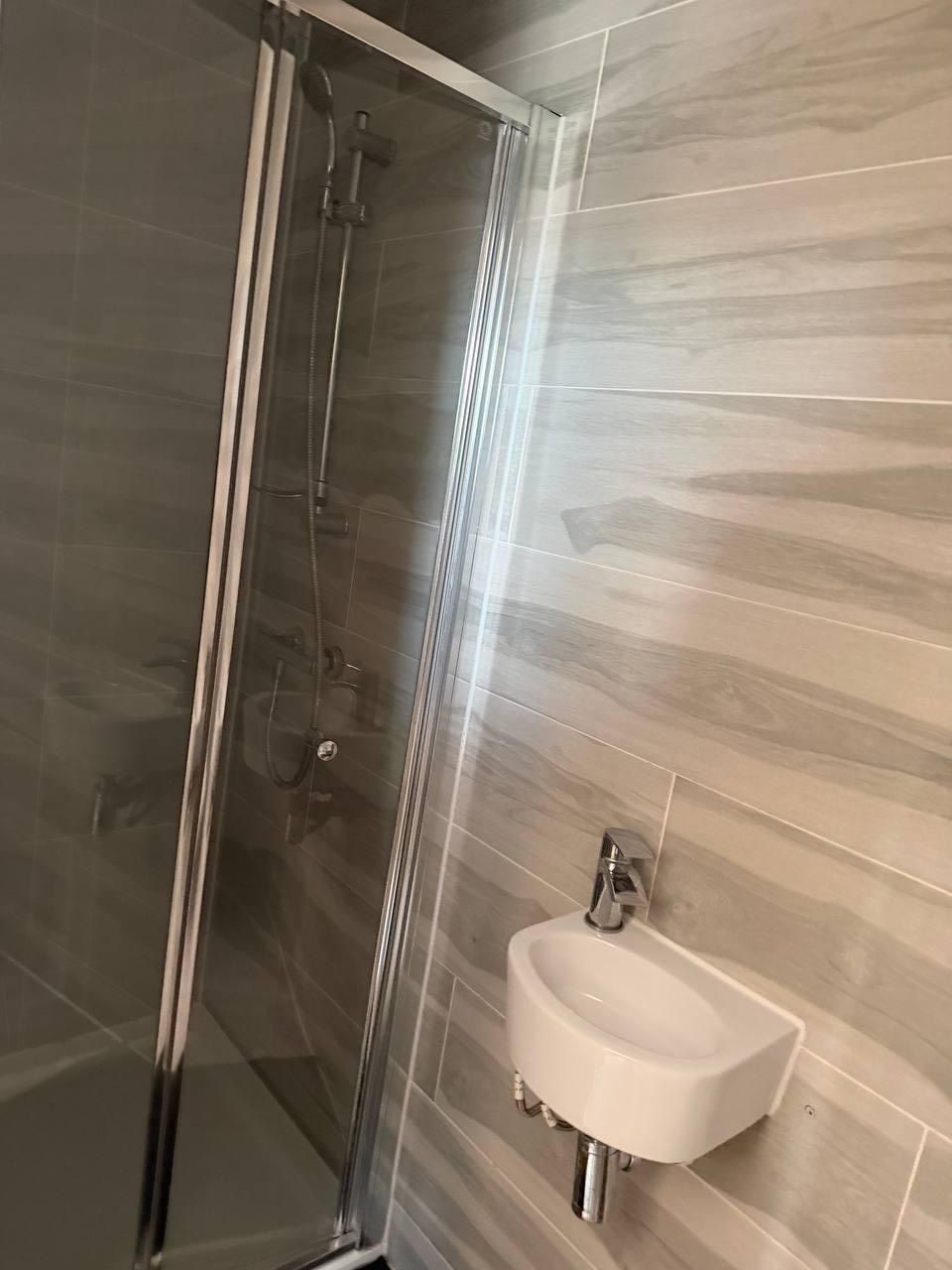 A shower enclosure with a glass door and a wall-mounted sink.