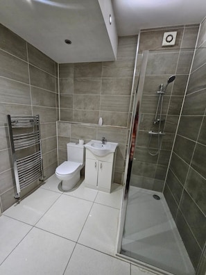 A modern bathroom with a toilet, sink, and shower. - House Sleeps 10 with Hot Tub and Garden (Romford)