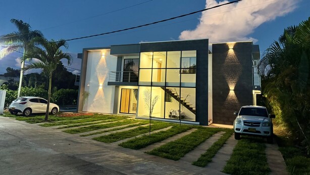 Una casa moderna de dos pisos con una escalera visible que conduce al nivel superior, un coche aparcado en la entrada y un césped bien cuidado.