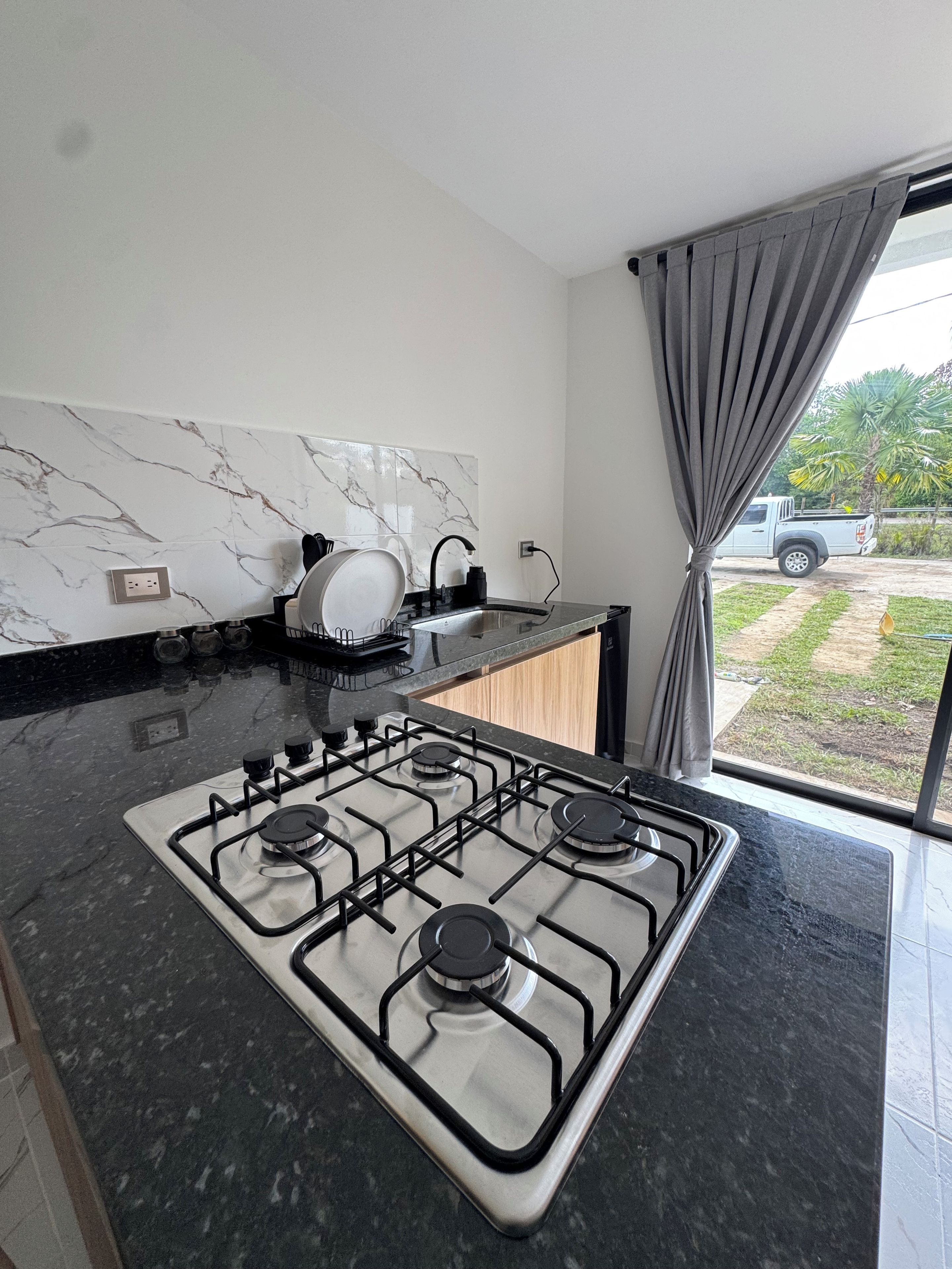 A modern kitchen with a gas stove, marble backsplash, and a view of the outdoors.