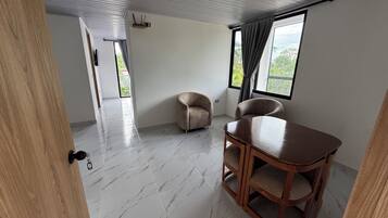 Una habitación amplia con una mesa de madera y dos sillas, un ventanal con cortinas y vistas a la vegetación.