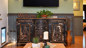 A living room with a wooden coffee table, a potted plant, a candle, and a wall-mounted flat-screen TV.