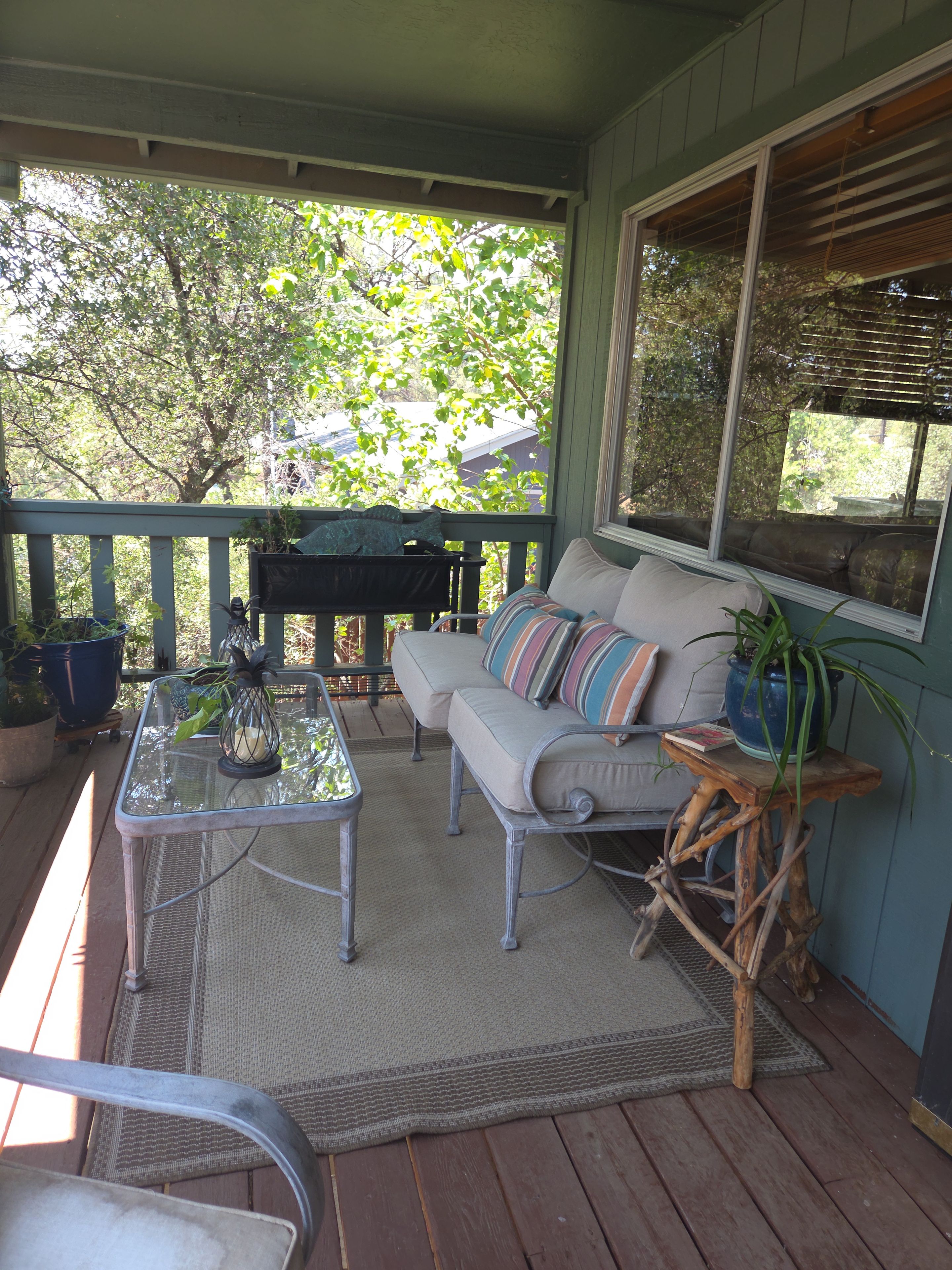 A covered porch with a sofa, a table, and a potted plant.