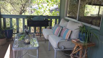 A covered porch with a sofa, a table, and a potted plant.