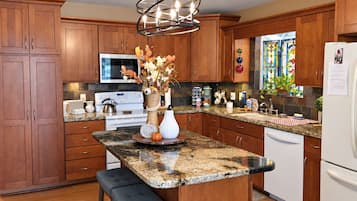 A kitchen with wooden cabinets, a granite countertop, a central island with a bench, and a stainless steel refrigerator.