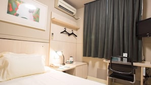 Ein Hotelzimmer mit Bett, Schreibtisch mit Stuhl, Klimaanlage, Fernseher und einem Fenster mit Vorhängen.