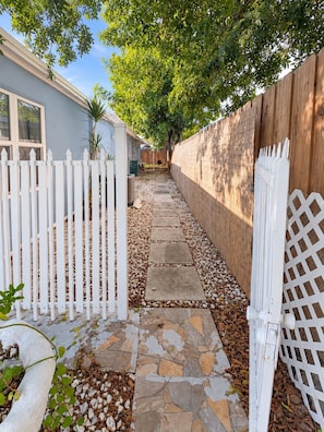A pathway leading to a house with a white picket fence, a wooden fence, and a stone-tiled walkway.