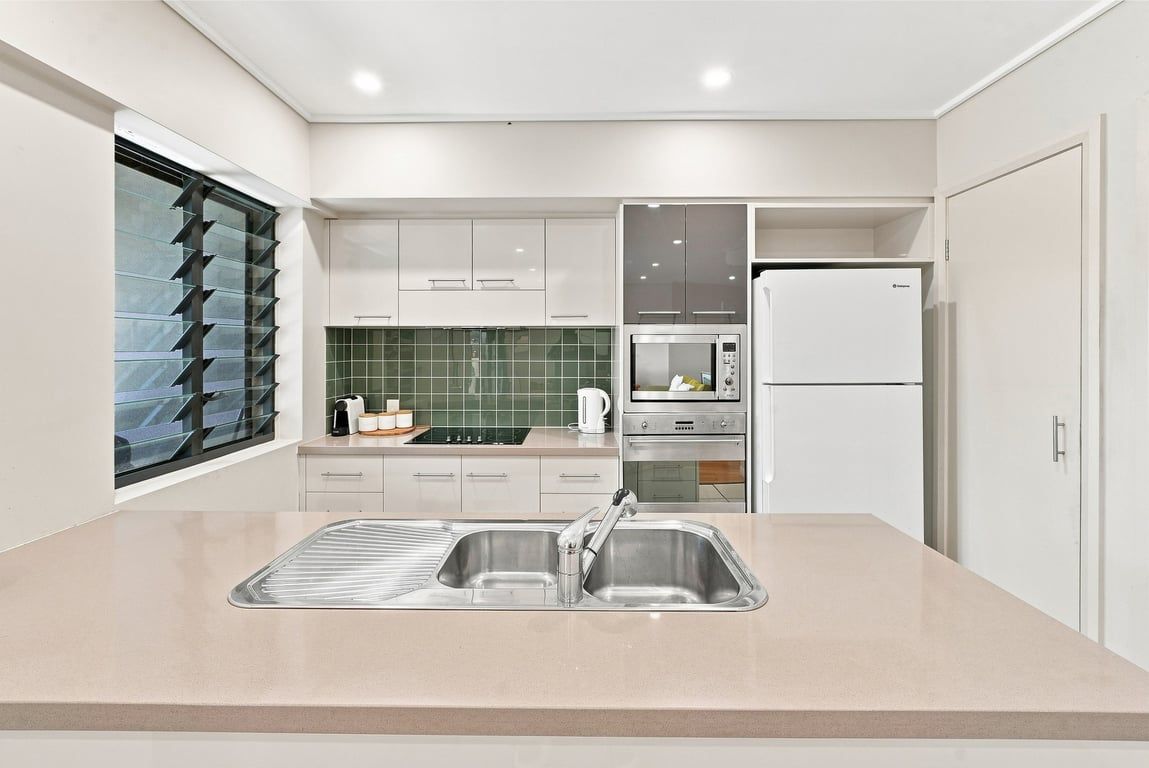 A modern kitchen with a double sink, stainless steel appliances, and a green tiled backsplash.