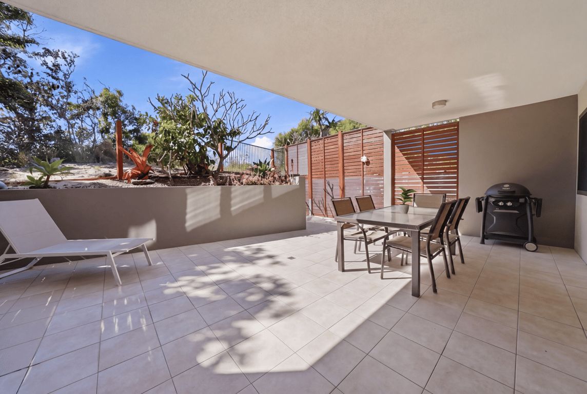 A patio with a table and chairs, a grill, and a lounge chair.