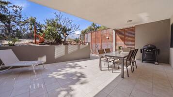 A patio with a table and chairs, a grill, and a lounge chair.