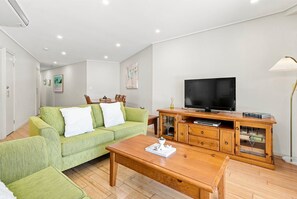 A living room with a green sofa, wooden coffee table, and a TV on a wooden cabinet.