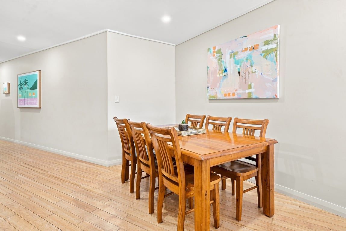 A dining area with a wooden table and chairs, a painting on the wall, and a framed picture.