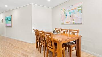 A dining area with a wooden table and chairs, a painting on the wall, and a framed picture.
