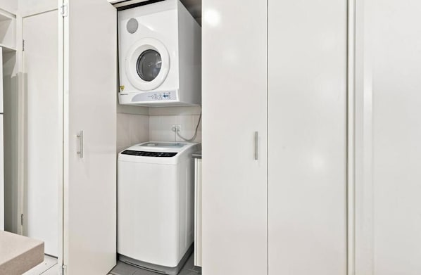 A compact laundry room with a front-loading washing machine and a top-loading dryer.