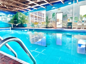 Une piscine intérieure à l’eau d’un bleu limpide, avec un escalier métallique et un sol carrelé.