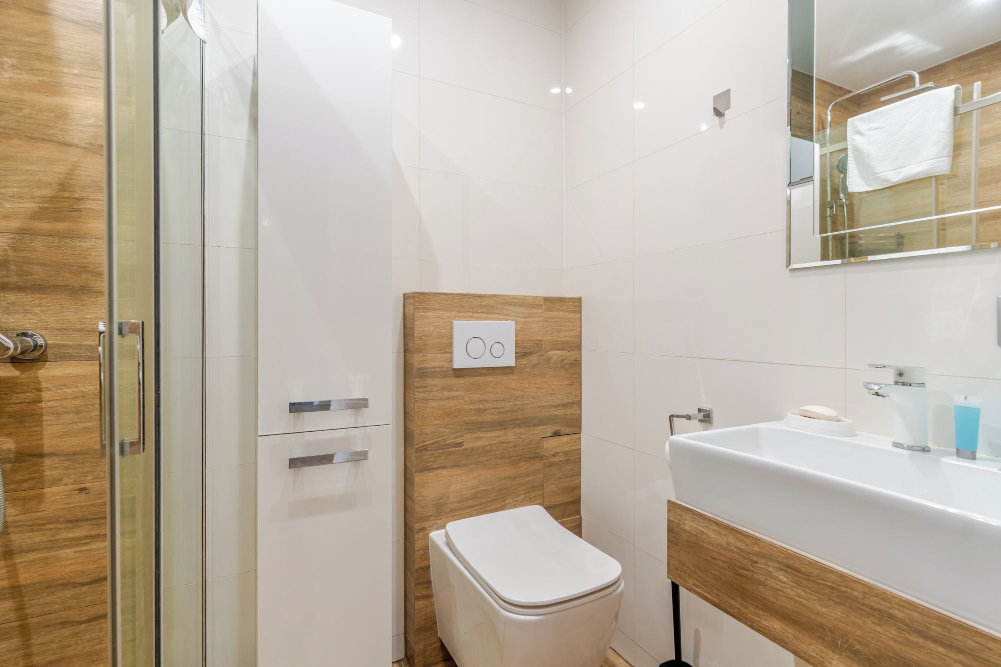 A modern bathroom with a glass shower enclosure, a white toilet, and a sink with a wooden vanity.