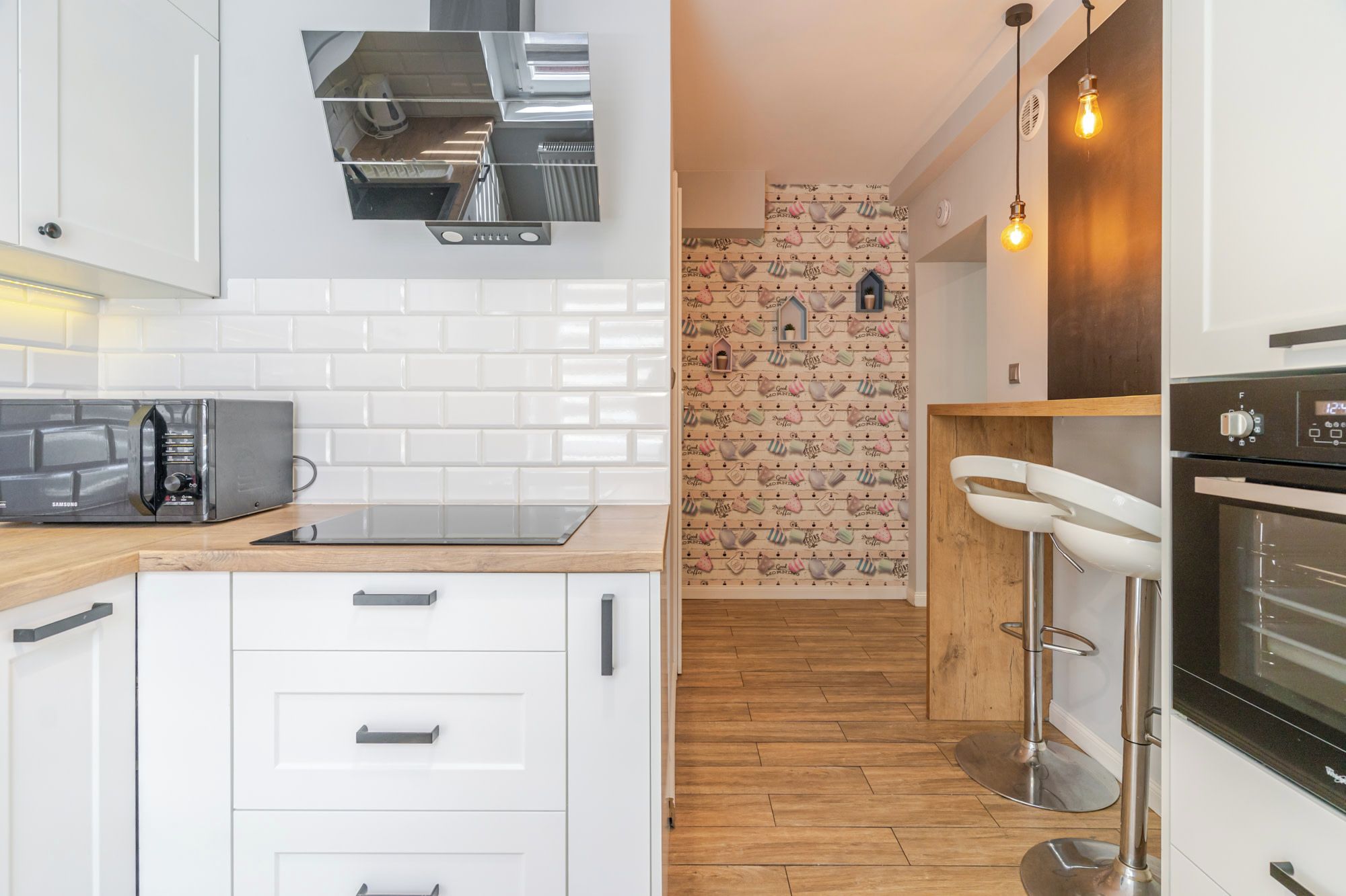 A modern kitchen with white cabinets, a built-in microwave, a wooden countertop, and a brick-patterned backsplash.