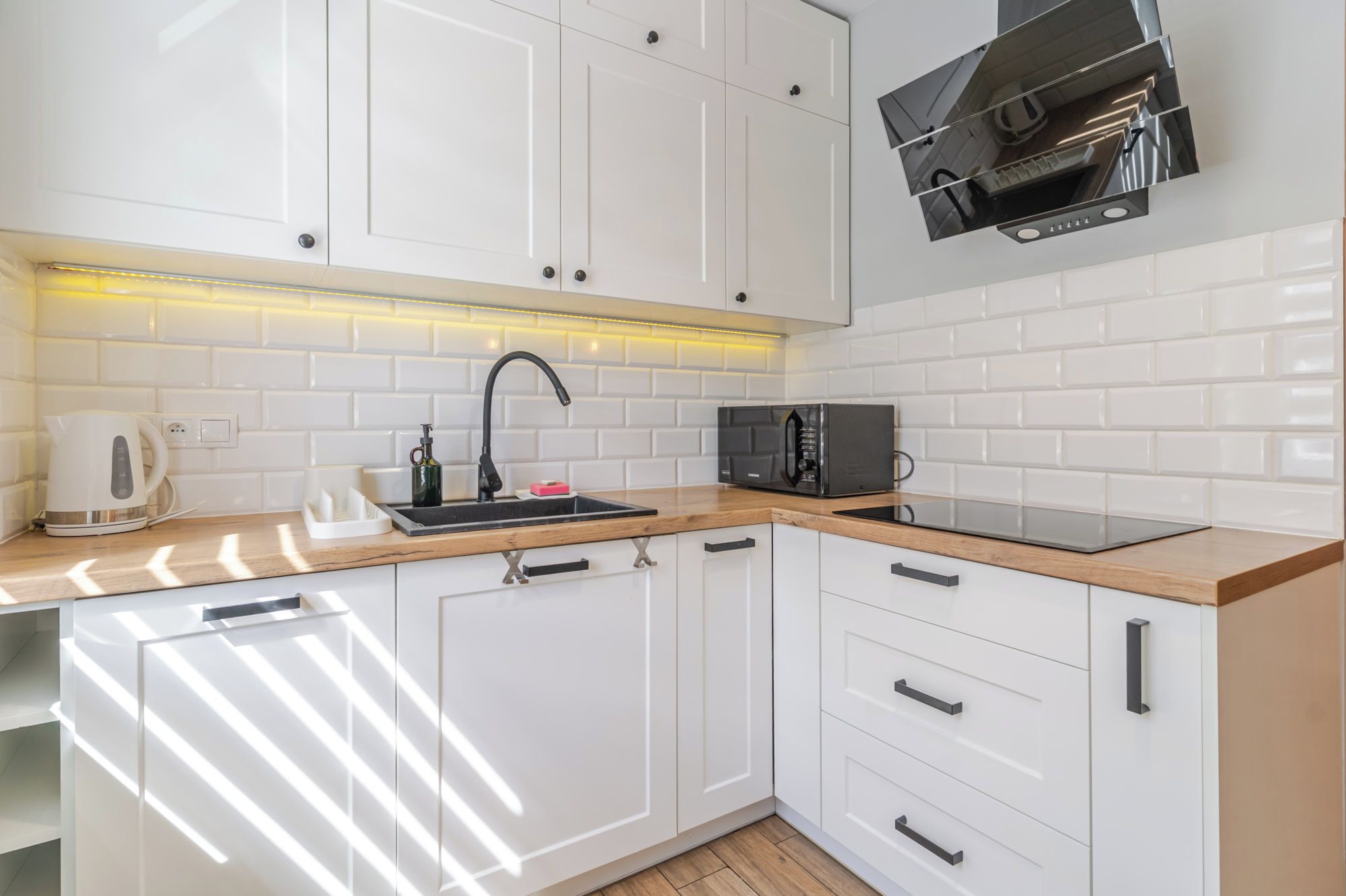 A modern kitchen with white cabinets, a black microwave, and a built-in oven.