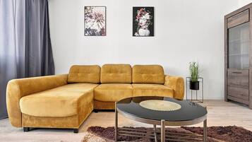 Una sala de estar moderna con un sofá seccional color mostaza, una mesa de centro redonda negra y dos cuadros con motivos florales en la pared.