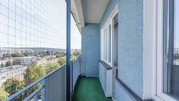 Un balcó estret amb un paviment de gespa artificial verda, barana de metall i vista d'un paisatge urbà amb edificis i arbres.
