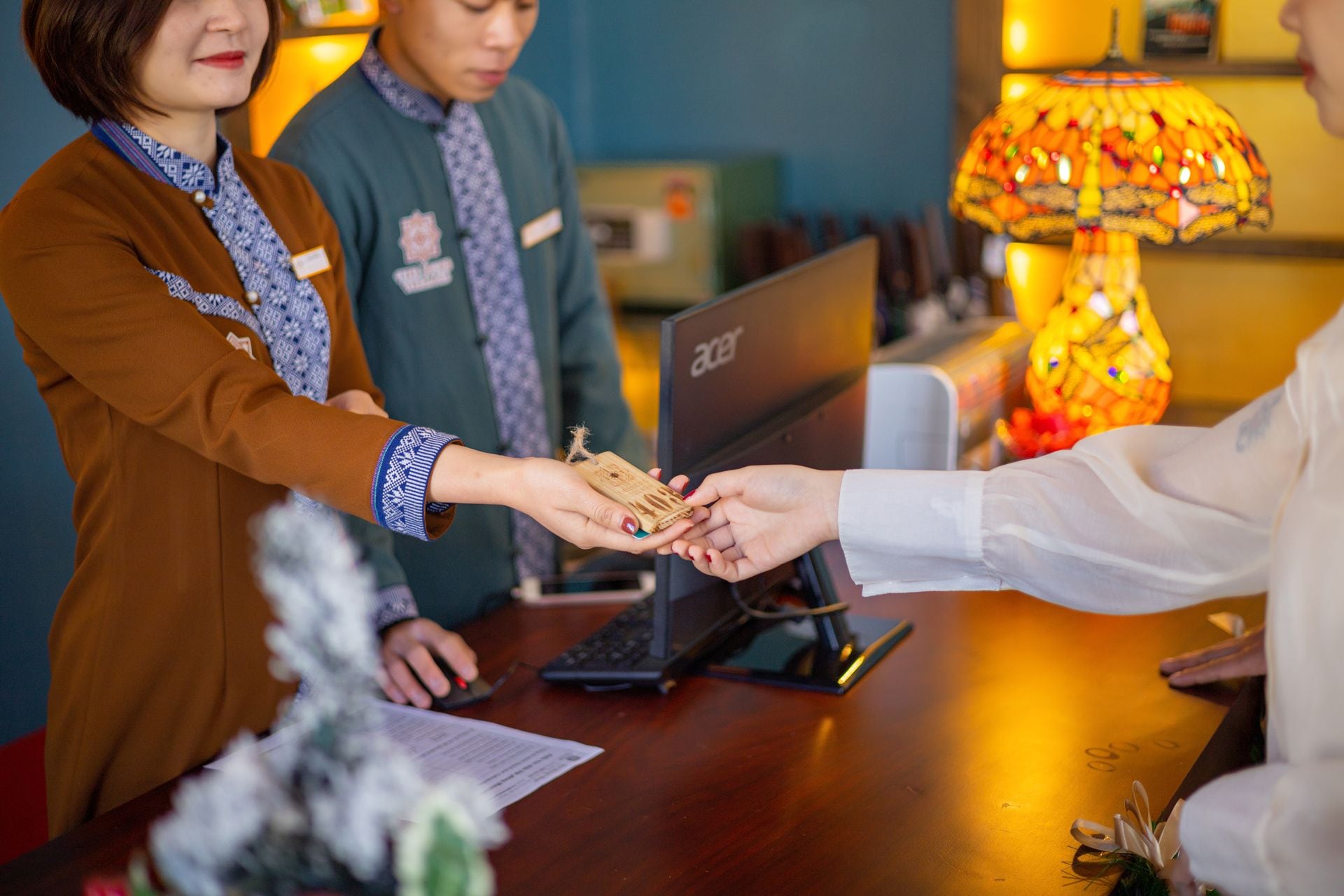 A hotel reception desk with a computer, a lamp, and a small plant.