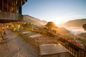 Una terraza de madera con bancos que ofrece vistas a un paisaje montañoso durante el amanecer.