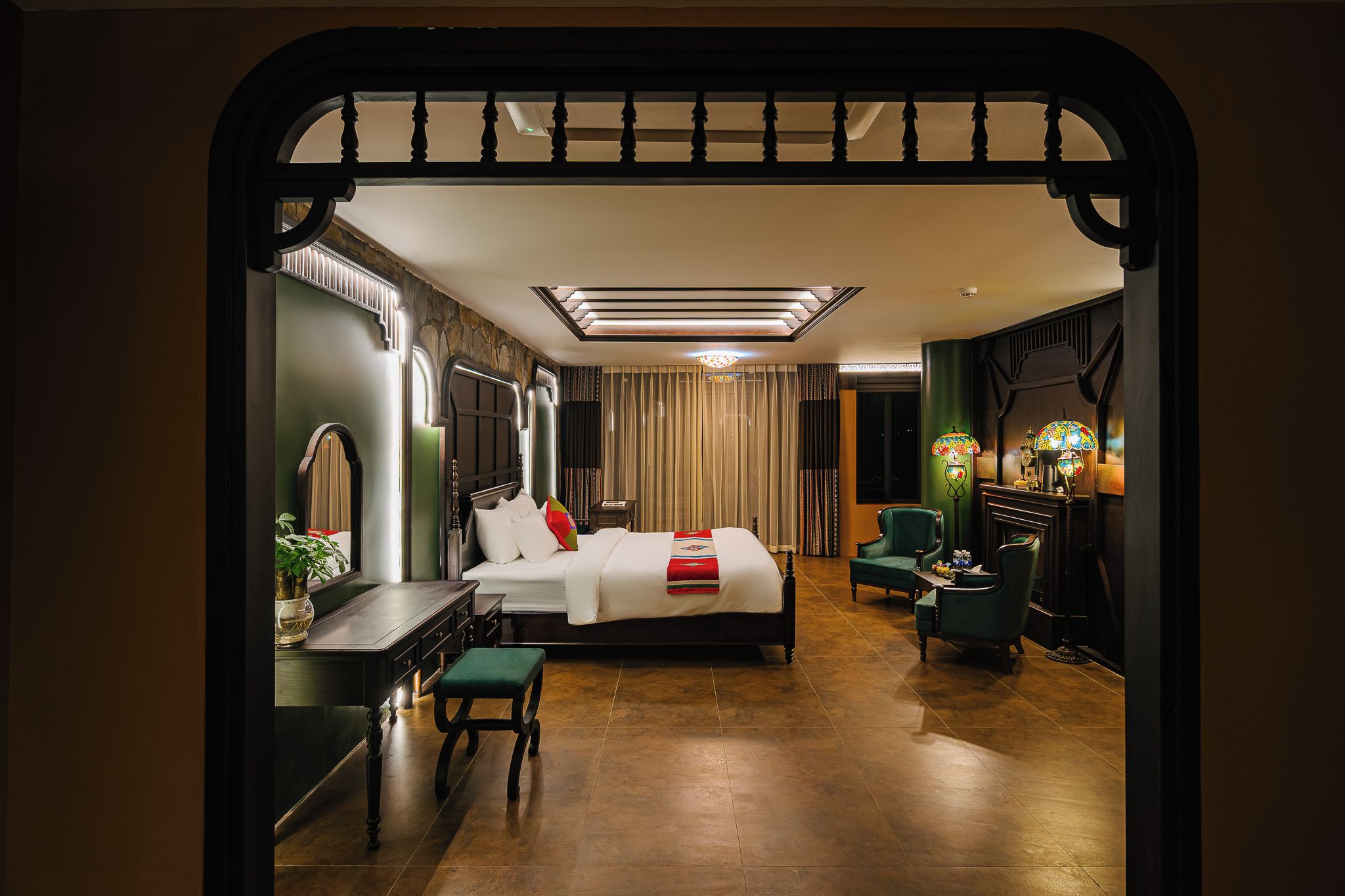 A hotel room with a bed, a desk, a chair, a lamp, and a fireplace.