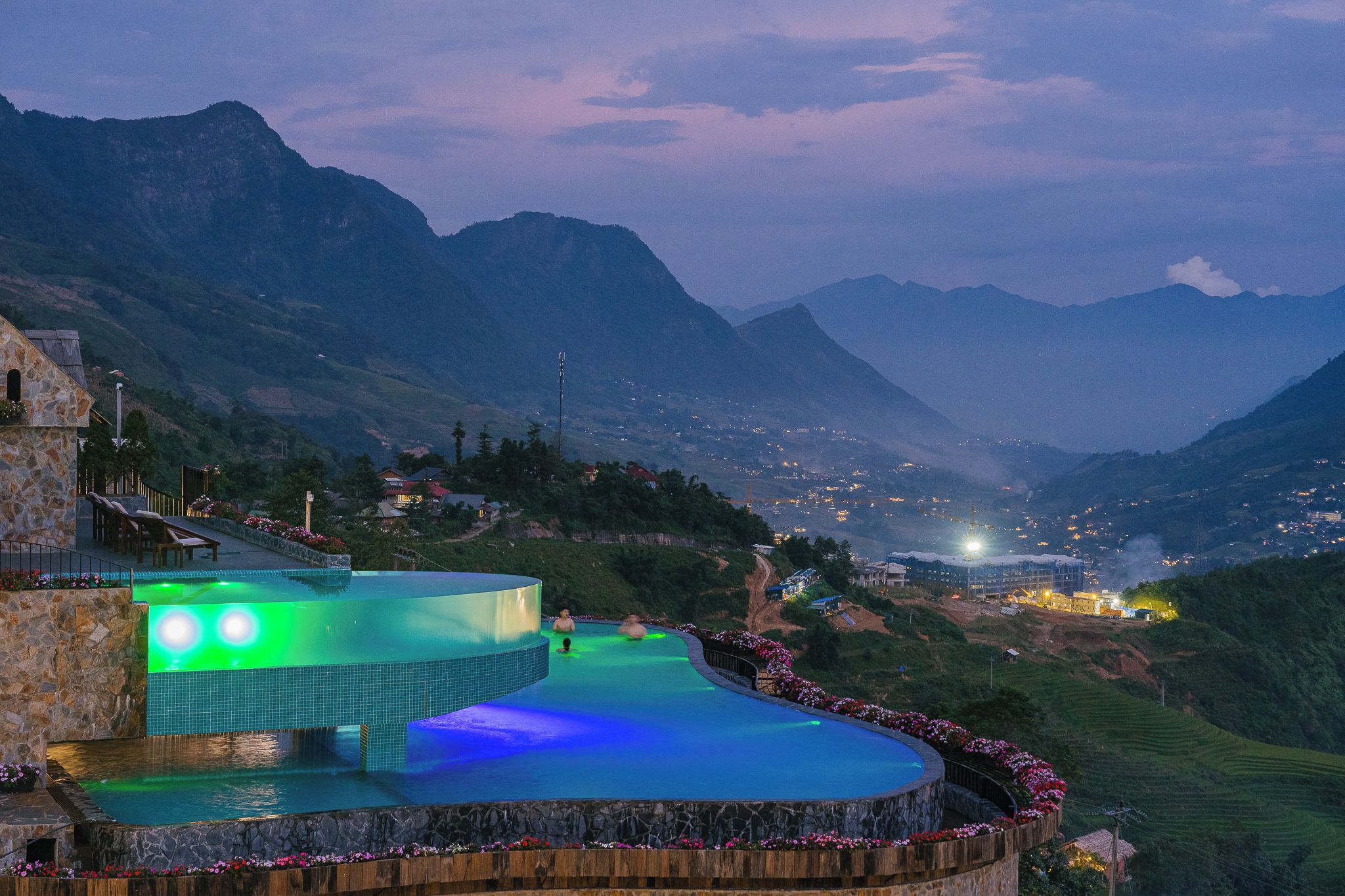 Una piscina con borde curvo, rodeada por un muro de piedra y una cubierta de madera, con montañas al fondo.