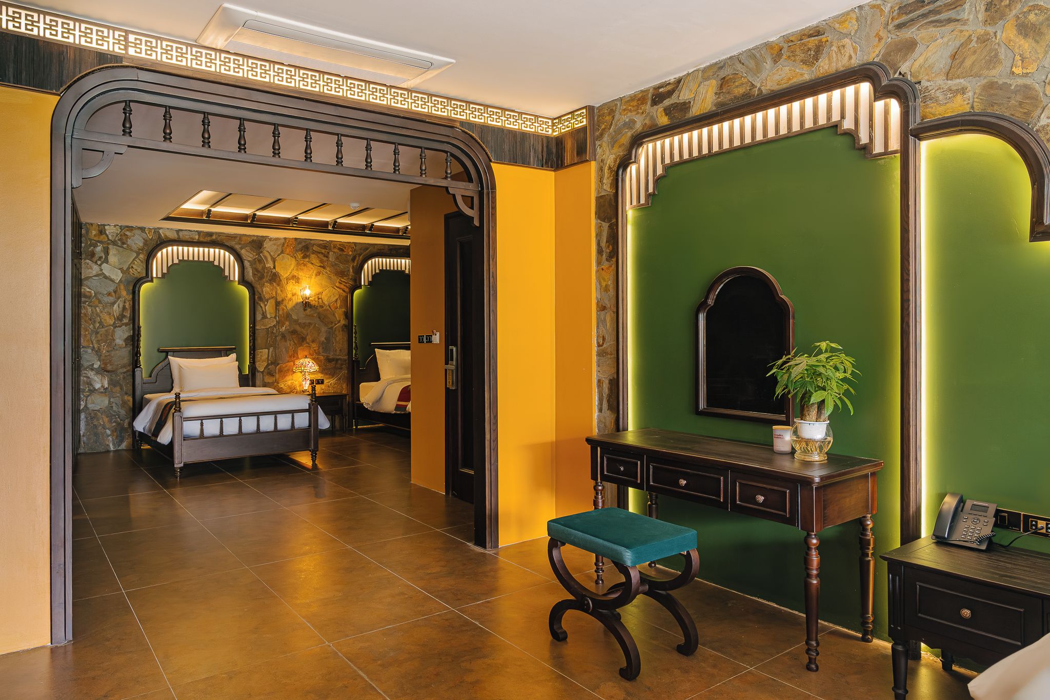 Une chambre d’hôtel avec un lit, un bureau avec un téléphone, une chaise et un mur vert agrémenté d’un miroir.