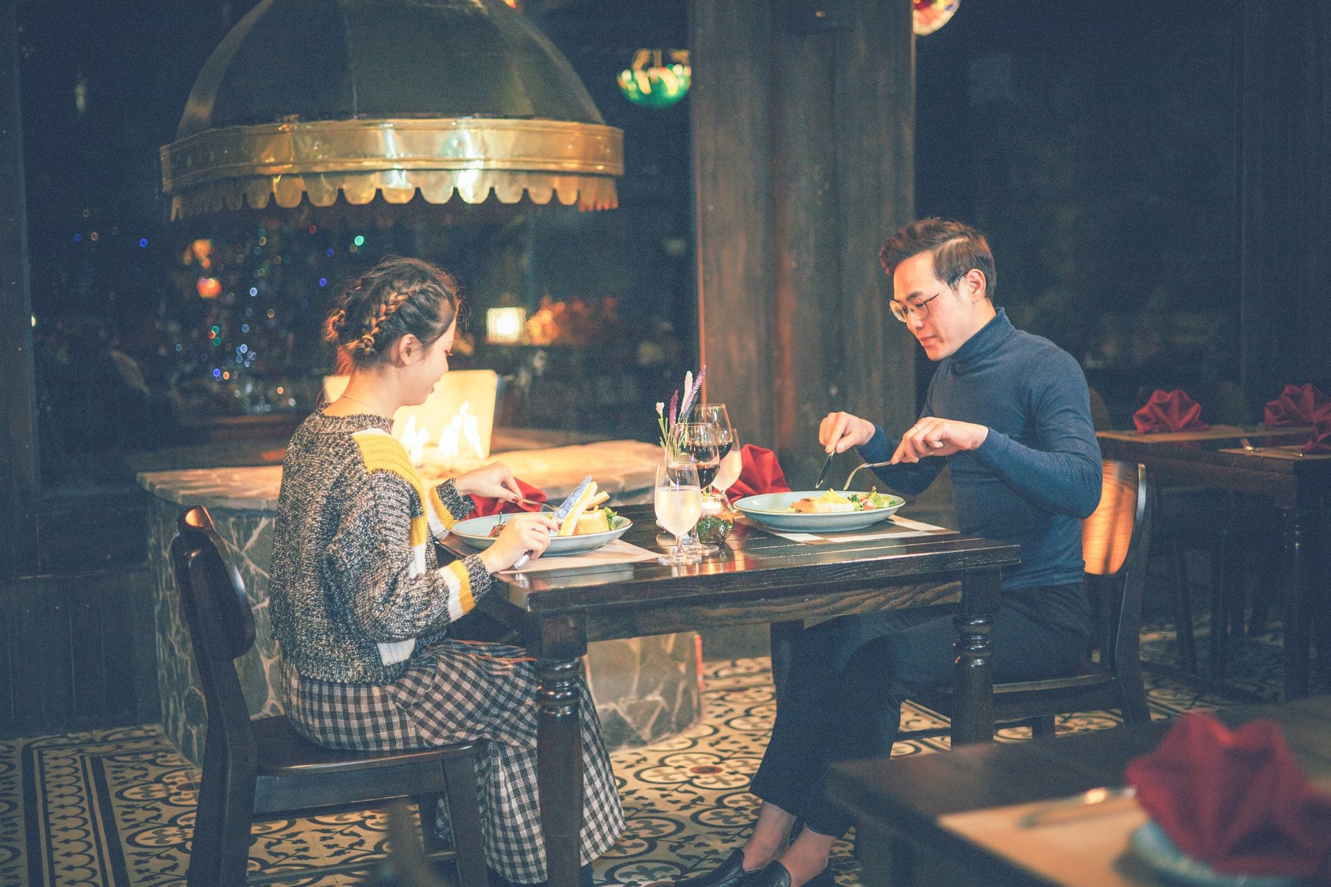 A dining table with two people seated, a bottle of wine, and a glass of water.