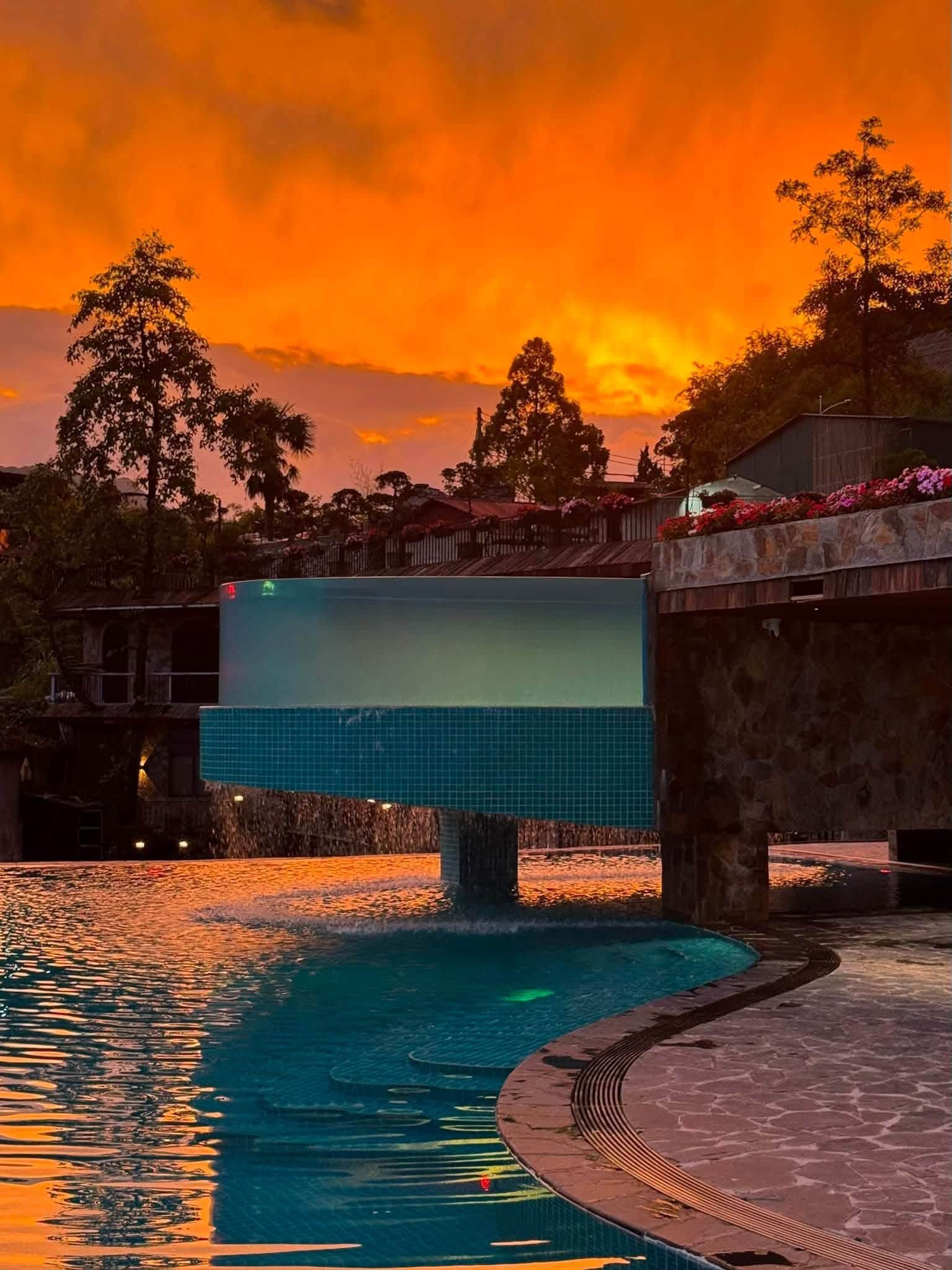 A swimming pool with a sunset view, surrounded by trees and a stone wall.