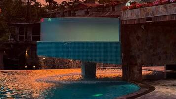 A swimming pool with a sunset view, surrounded by trees and a stone wall.