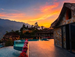 Un resort con piscina, edificios de piedra y montañas al fondo.