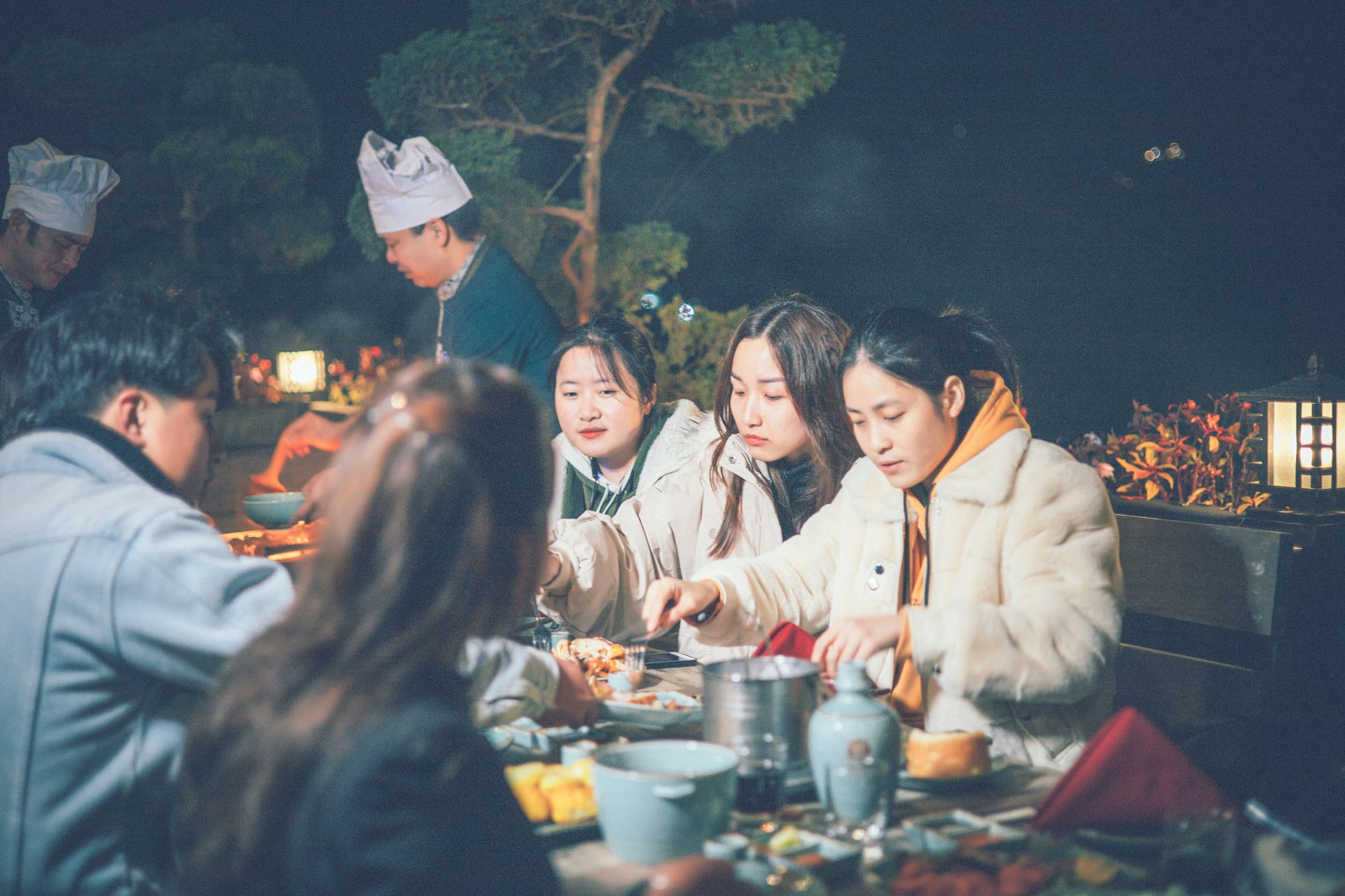 A group of people dining outdoors at night with a table set for a meal.