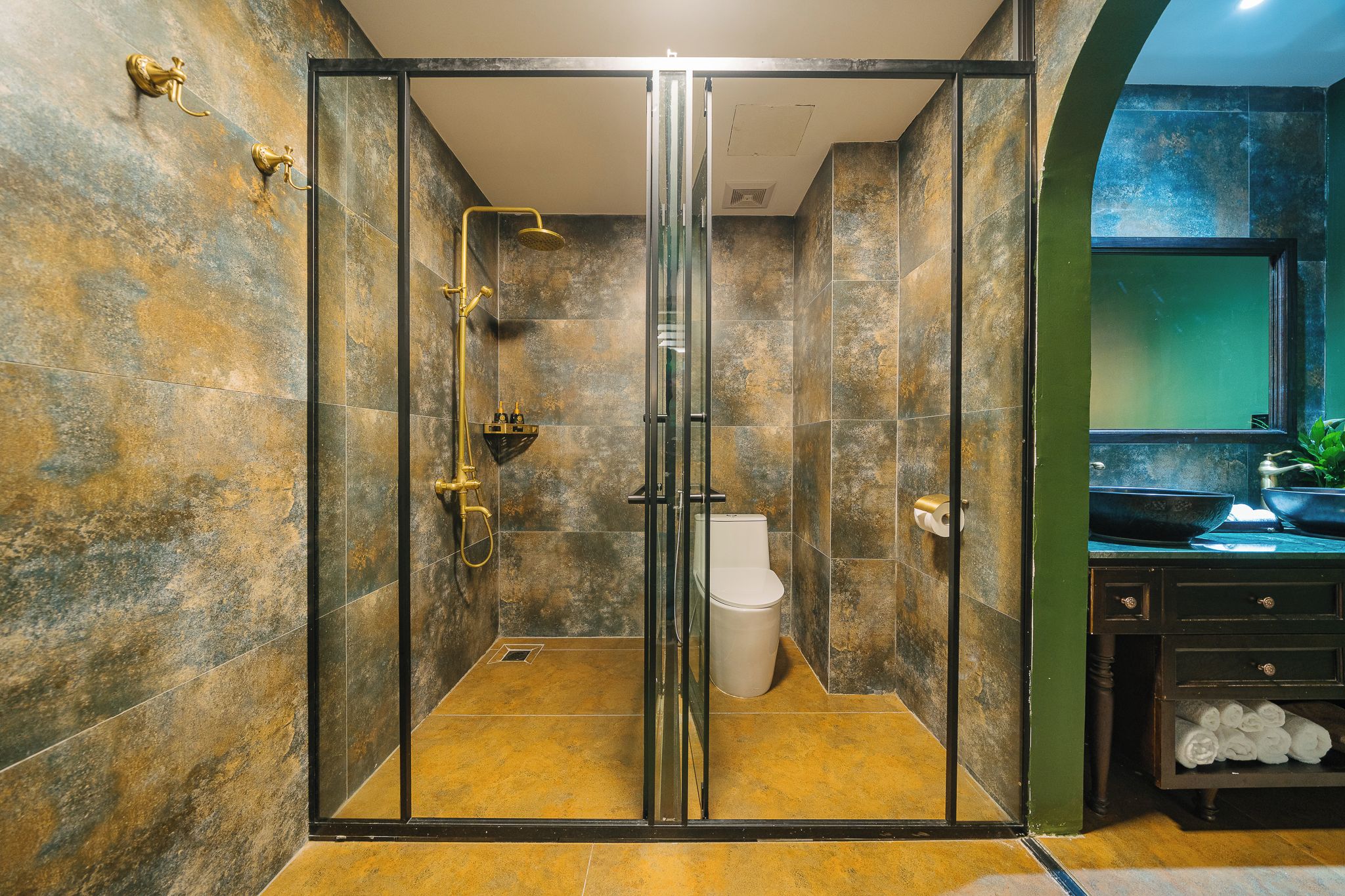 Un baño moderno con ducha envuelta en cristal, inodoro y lavamanos con pared verde y ventana.