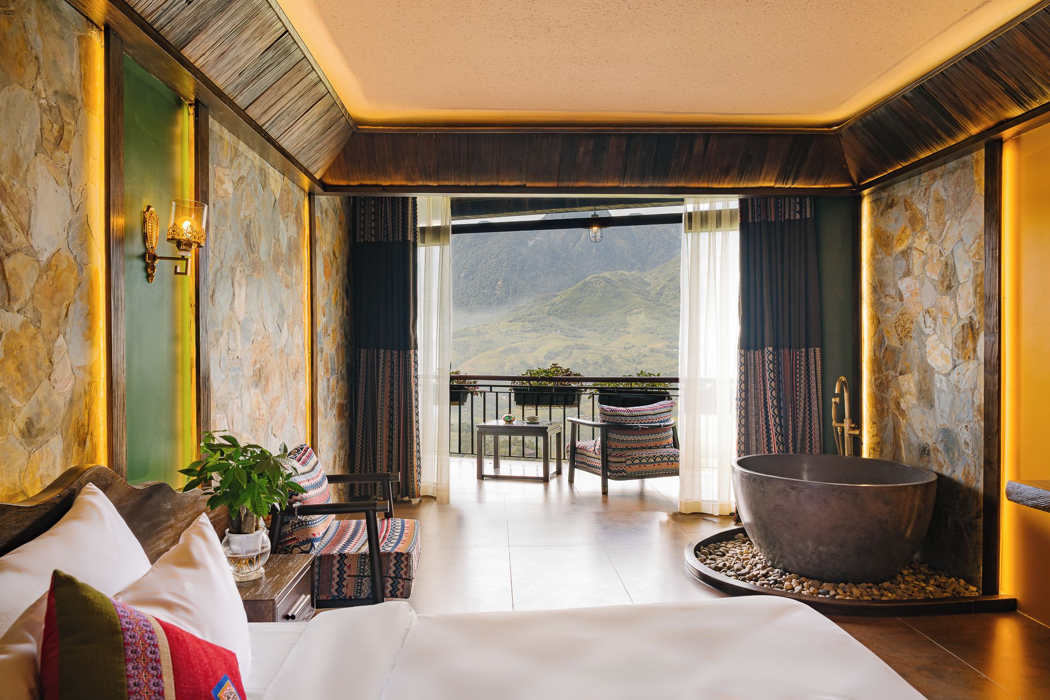 Habitación de hotel con una cama grande, una bañera, un balcón con vistas a las montañas y un comedor.