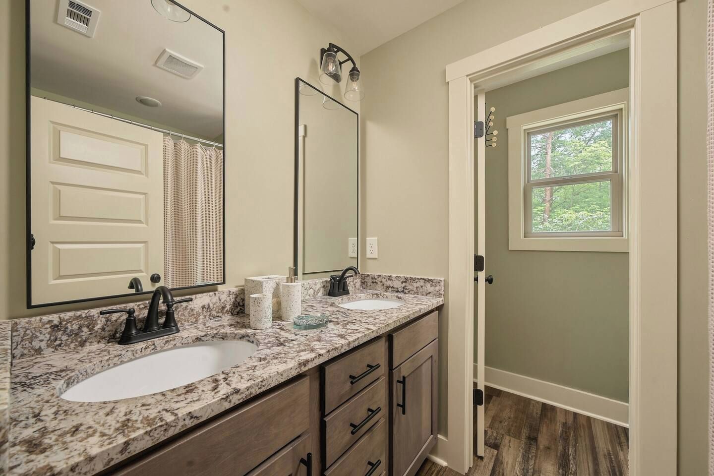 A bathroom with two sinks, a large mirror, and a door leading to a room with a window.