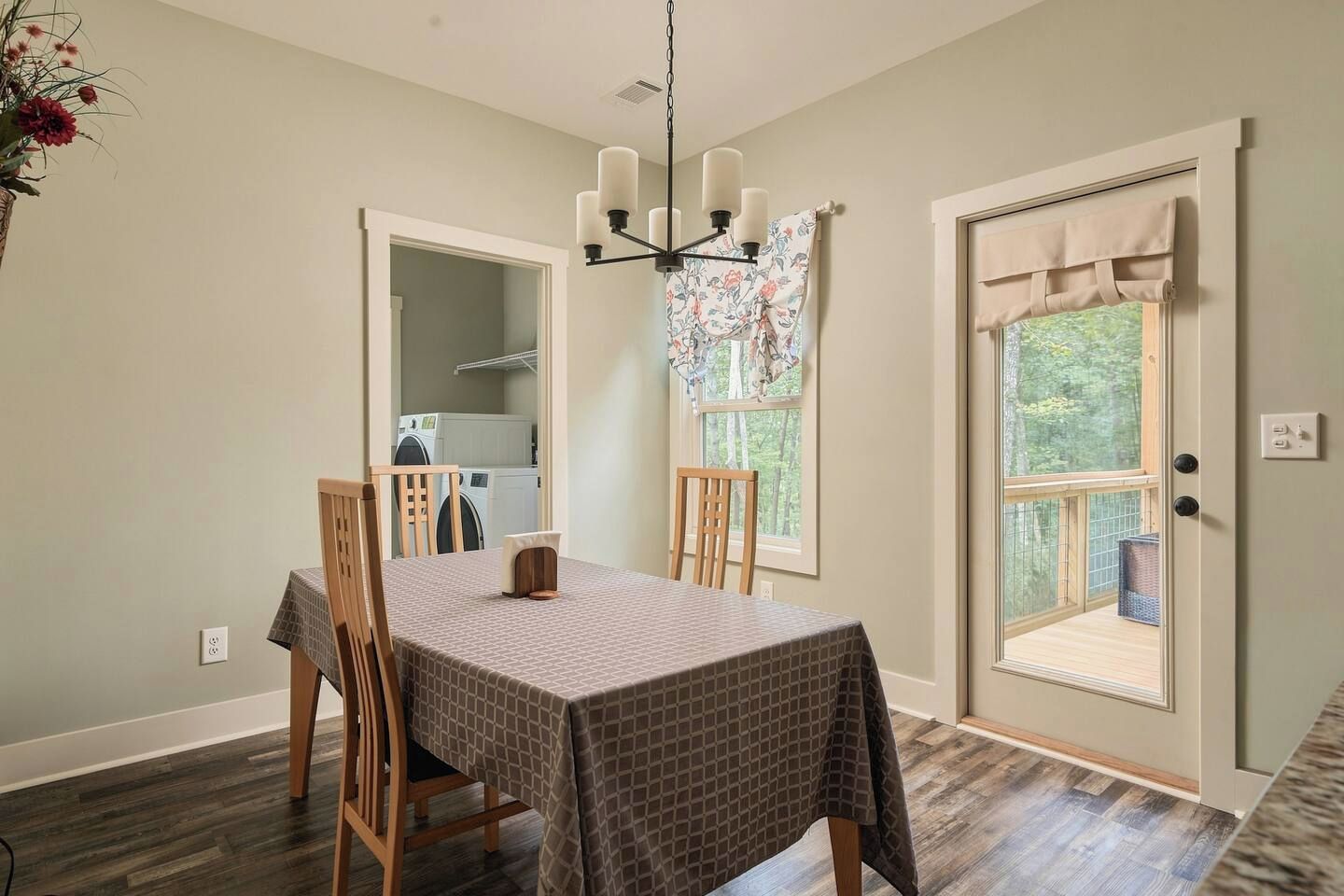 A dining area with a table set for four, a chandelier, and a view of a laundry room through an open door.
