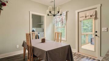 A dining area with a table set for four, a chandelier, and a view of a laundry room through an open door.