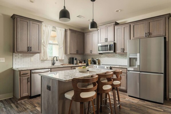 Una cocina moderna con armarios de madera oscura, electrodomésticos de acero inoxidable, encimera de granito y una isla central con taburetes de bar.