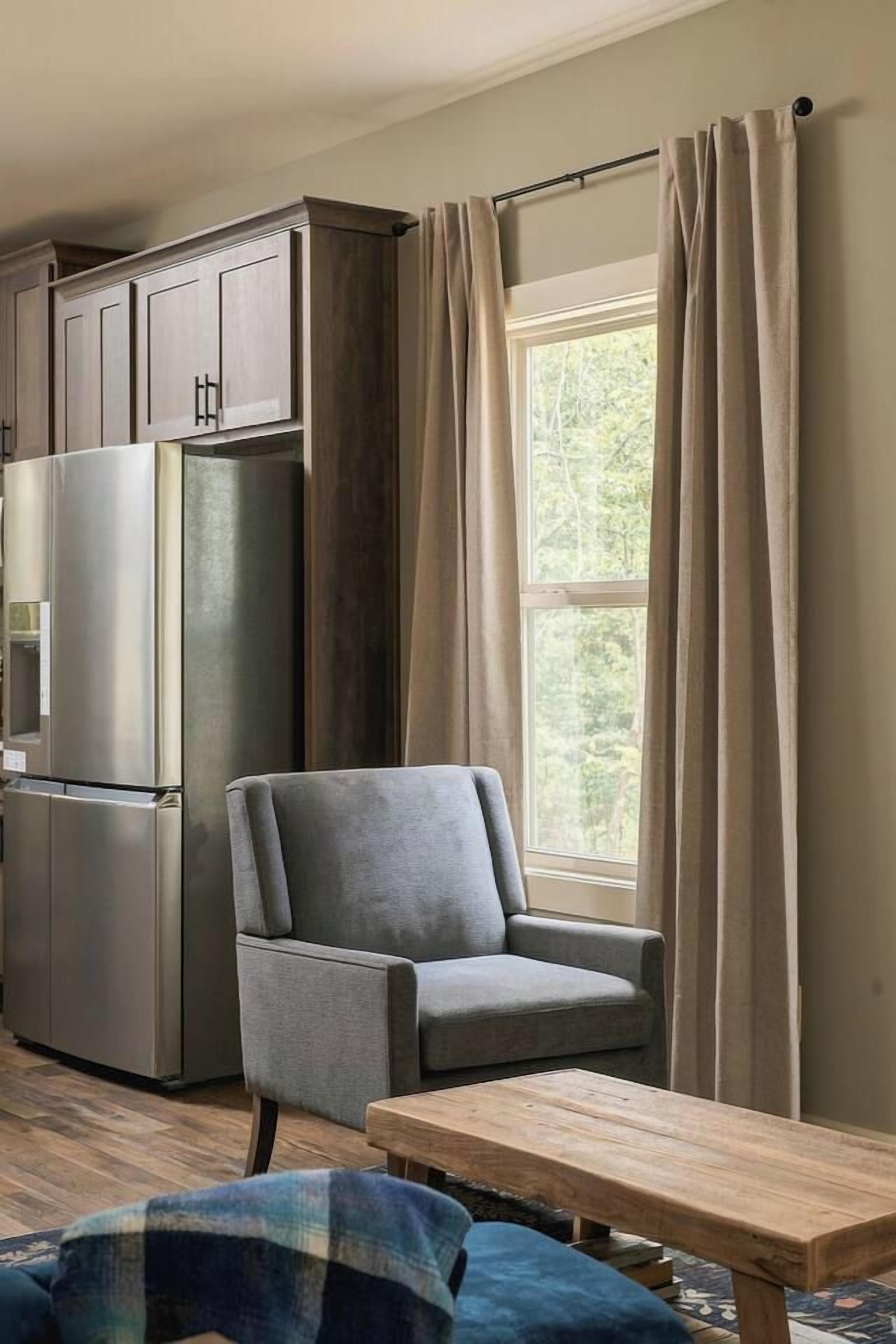 A living room with a grey armchair, a wooden coffee table, and a large window with curtains.