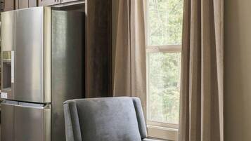 A living room with a grey armchair, a wooden coffee table, and a large window with curtains.