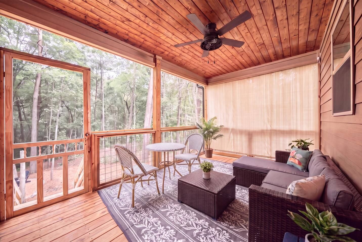 Eine Holzterrasse mit Deckenventilator, Korbmöbeln und Blick auf den Wald.