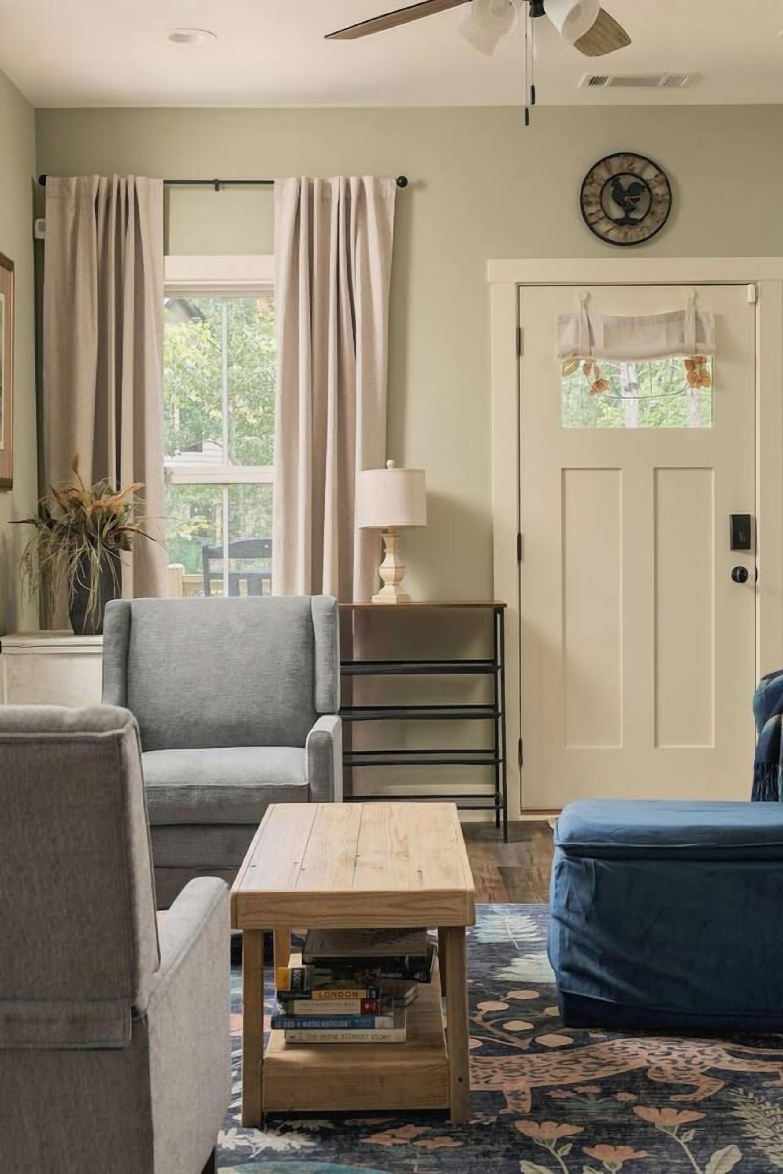 En stue med en grå lænestol, et træbord med bøger, en blå sofa og en dør med vindue.